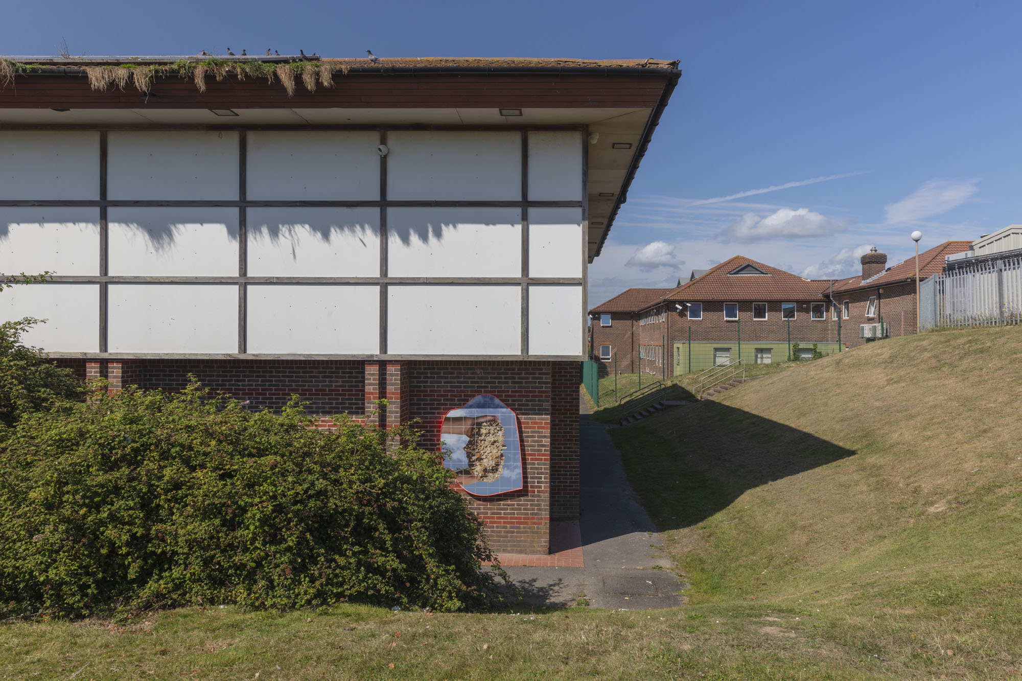 A photo of two hands holding a bronze object against a cloudy sky is printed onto tiles and embedded on the side of the exterior wall of Shinewater Sports Centre.
